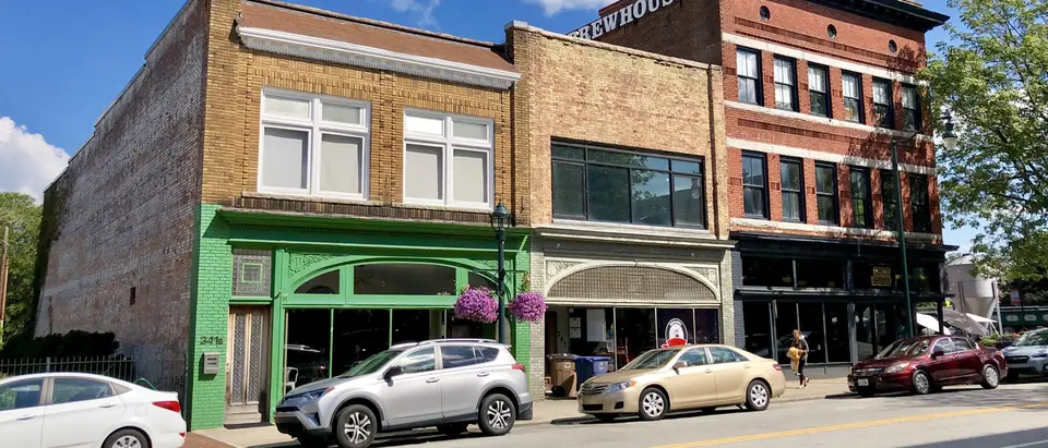 Historic brick storefronts along South Elm Street in downtown Greensboro, NC, under a blue sky