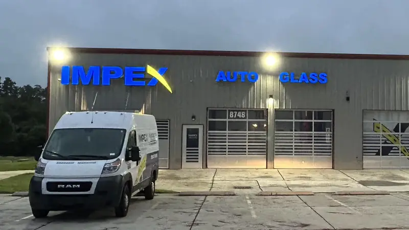 The Impex Auto Glass shop on West Market Street in Greensboro at dusk, with a service van out front